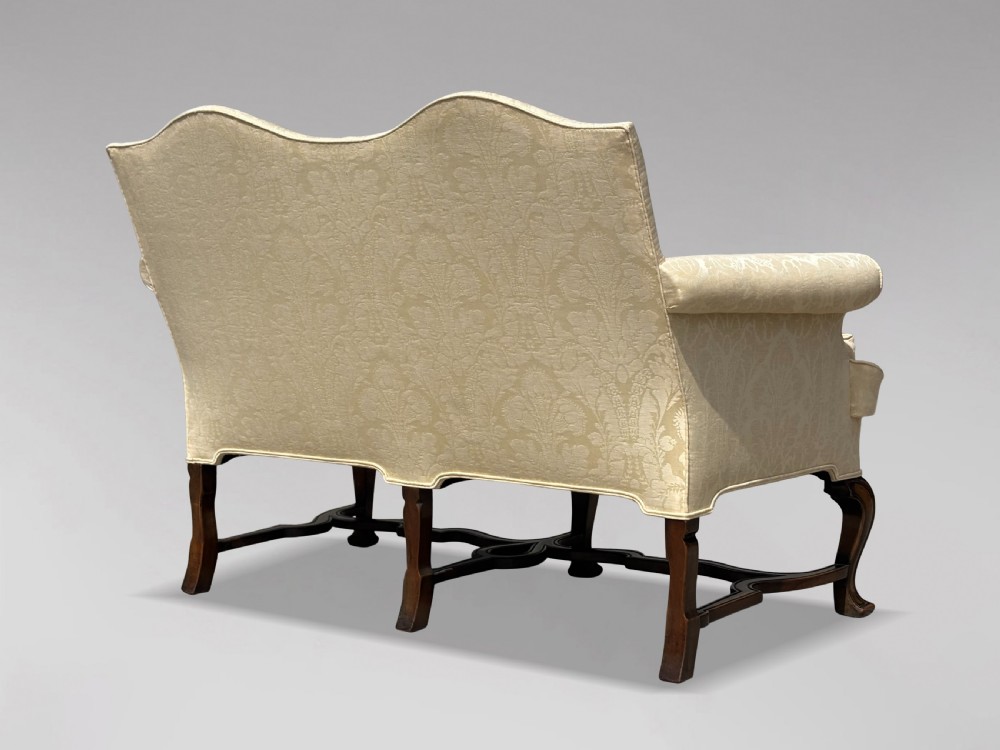 An Edwardian Queen Anne style settee upholstered in cream damask with carved walnut cabriole legs and a double-arched back. View VIII