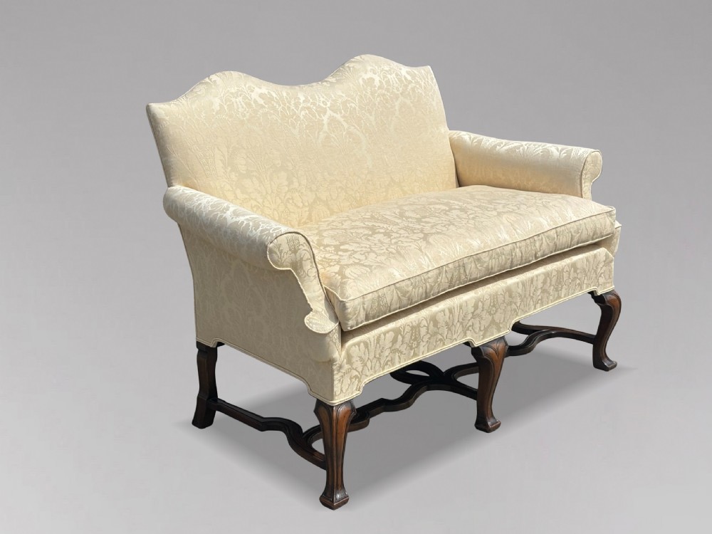 An Edwardian Queen Anne style settee upholstered in cream damask with carved walnut cabriole legs and a double-arched back. View IX