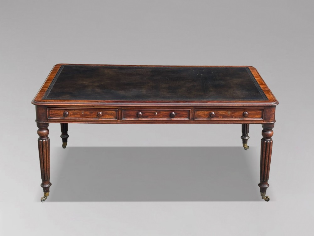An 18th-century mahogany library table featuring a black leather top insert, frieze drawers with wooden knob handles, and turned, fluted legs on brass castors. View II