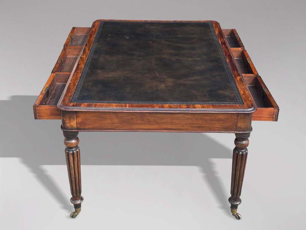 An 18th-century mahogany library table featuring a black leather top insert, frieze drawers with wooden knob handles, and turned, fluted legs on brass castors. View IV