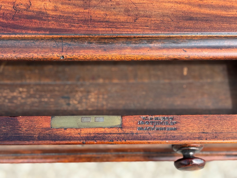 An 18th-century mahogany library table featuring a black leather top insert, frieze drawers with wooden knob handles, and turned, fluted legs on brass castors. View V