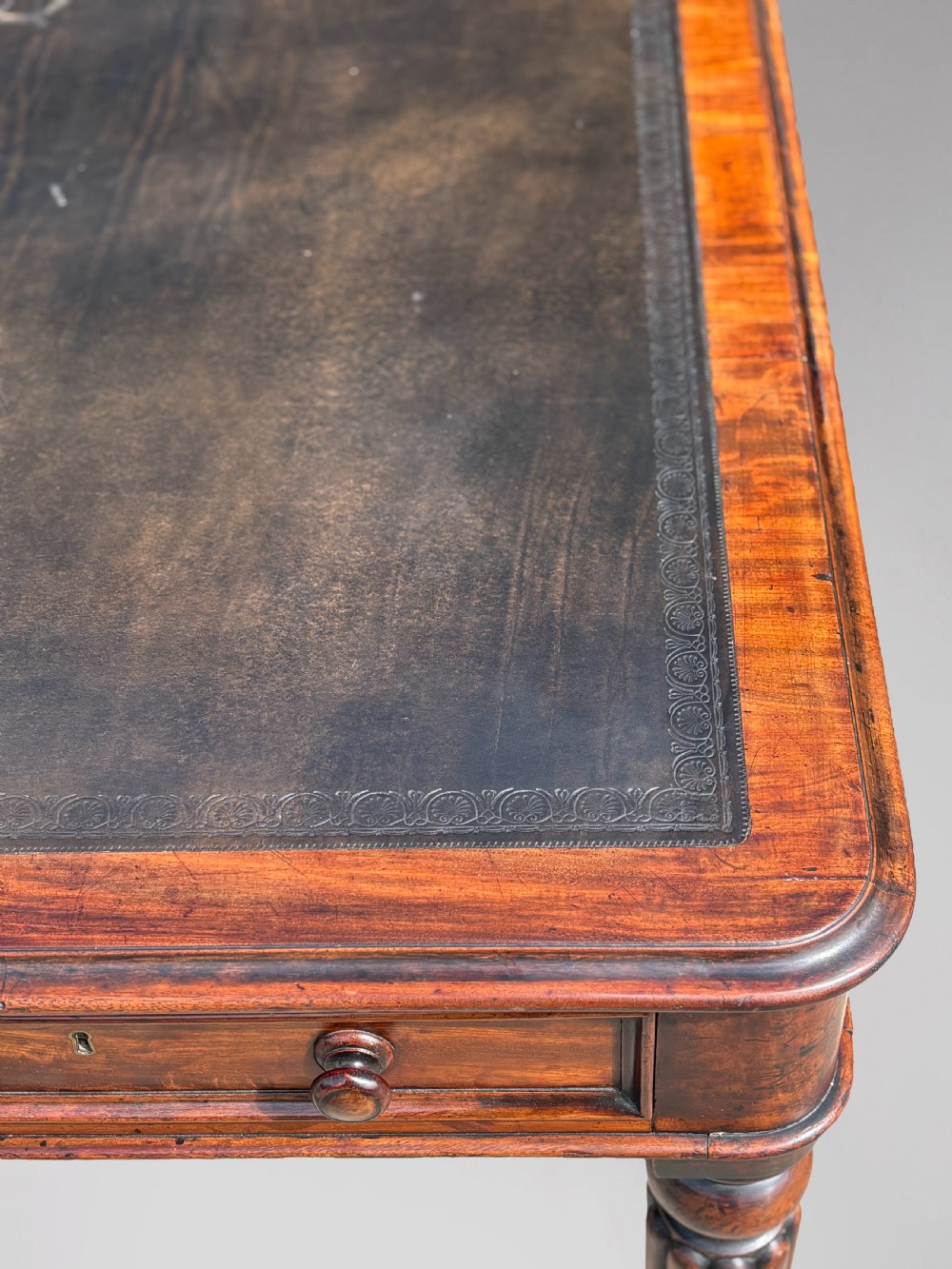 An 18th-century mahogany library table featuring a black leather top insert, frieze drawers with wooden knob handles, and turned, fluted legs on brass castors. View VII