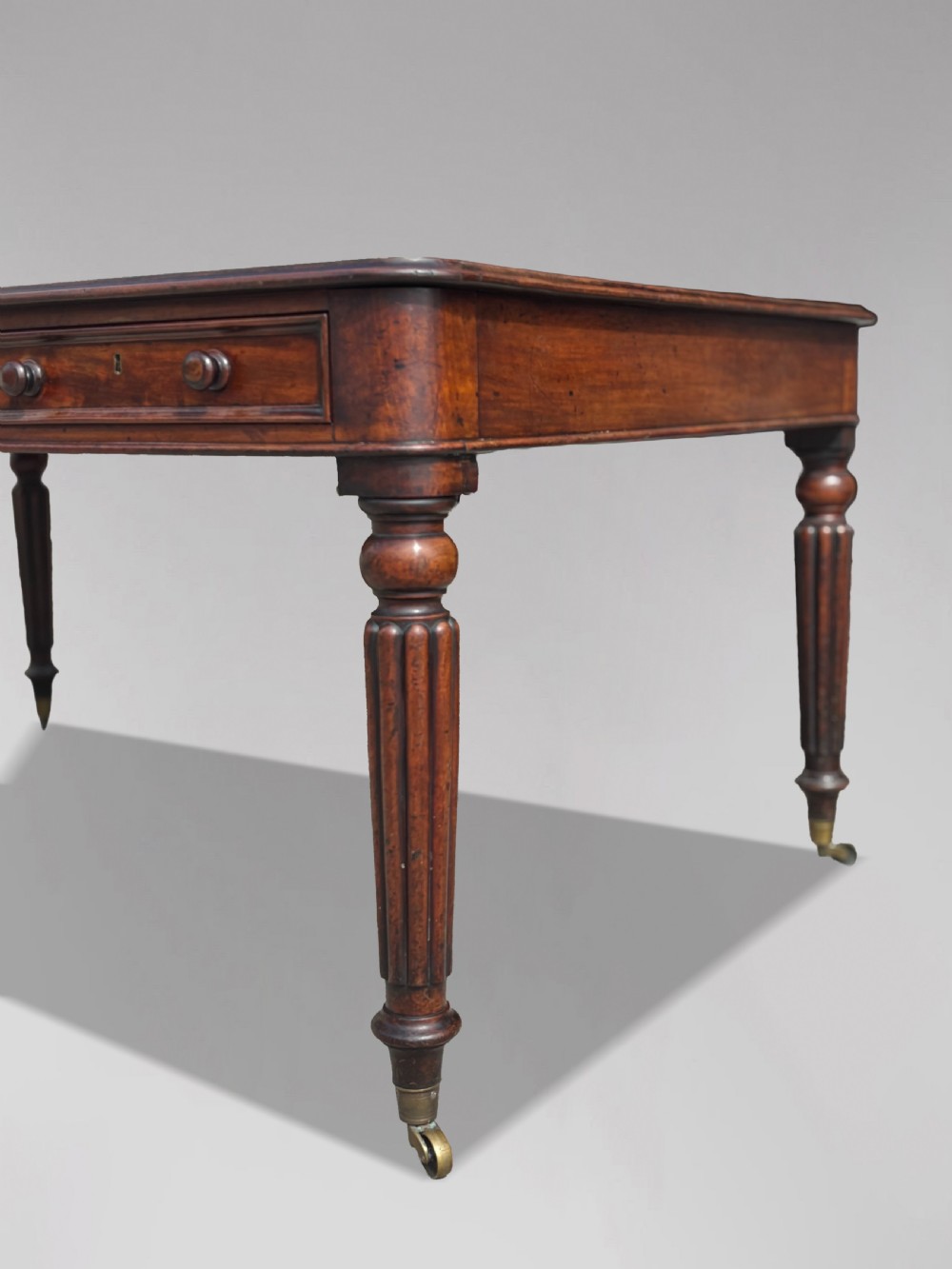 An 18th-century mahogany library table featuring a black leather top insert, frieze drawers with wooden knob handles, and turned, fluted legs on brass castors. View XII
