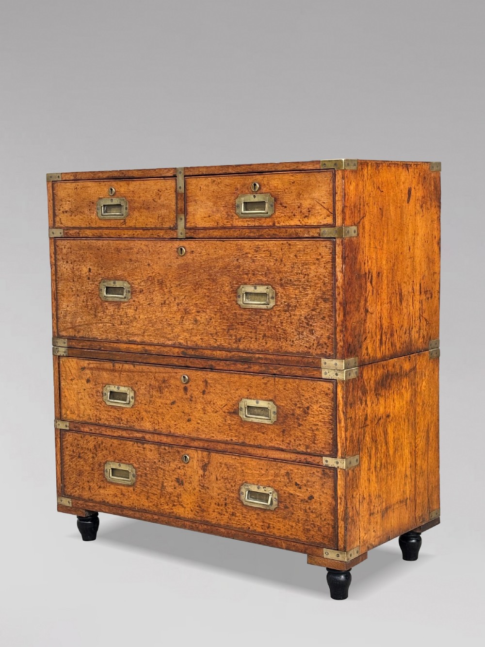 A nineteenth-century oak military campaign chest of drawers featuring brass corner straps, recessed flush handles, and turned feet.