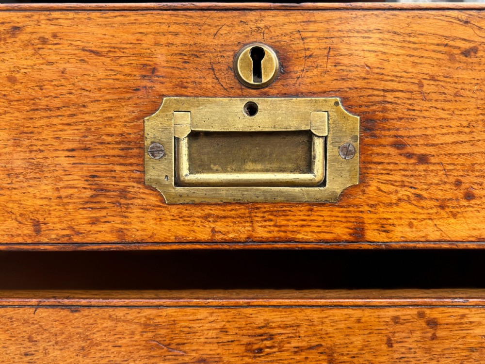 A nineteenth-century oak military campaign chest of drawers featuring brass corner straps, recessed flush handles, and turned feet. View XV