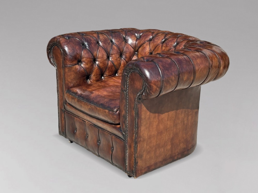An Edwardian brown leather Chesterfield armchair featuring deep button quilting, rolled arms, and stud trim details.