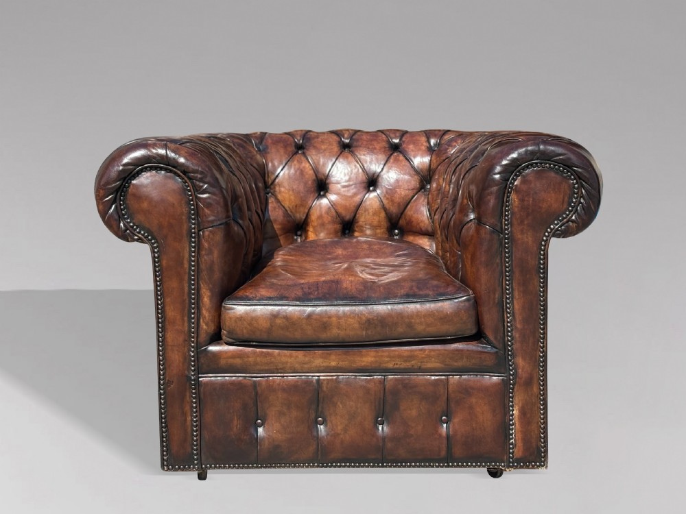 An Edwardian brown leather Chesterfield armchair featuring deep button quilting, rolled arms, and stud trim details. View II