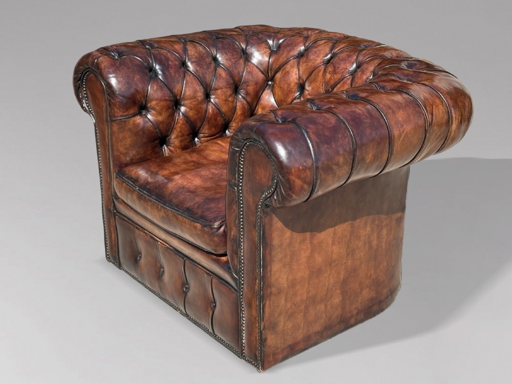 An Edwardian brown leather Chesterfield armchair featuring deep button quilting, rolled arms, and stud trim details. View IV