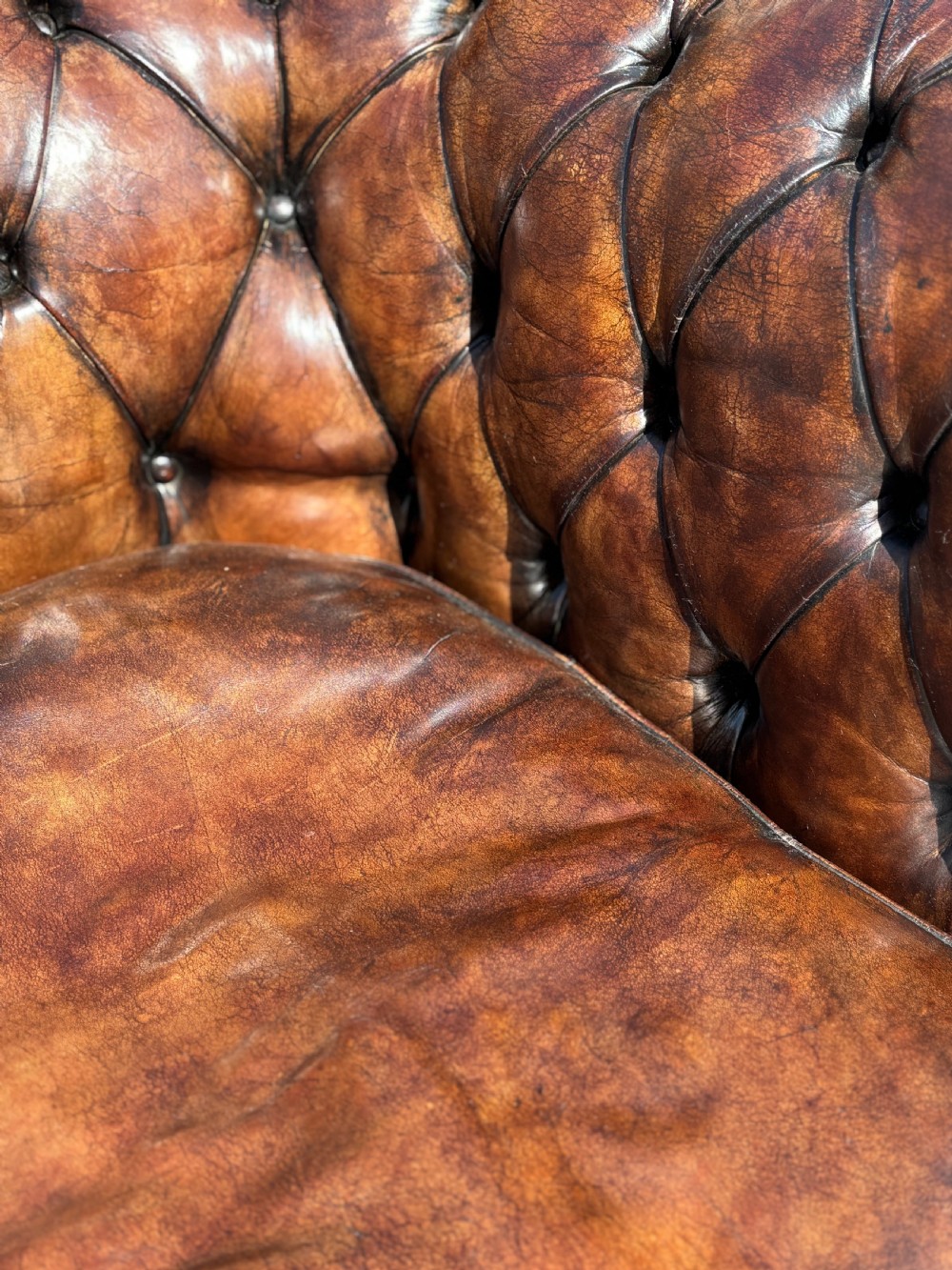 An Edwardian brown leather Chesterfield armchair featuring deep button quilting, rolled arms, and stud trim details. View V