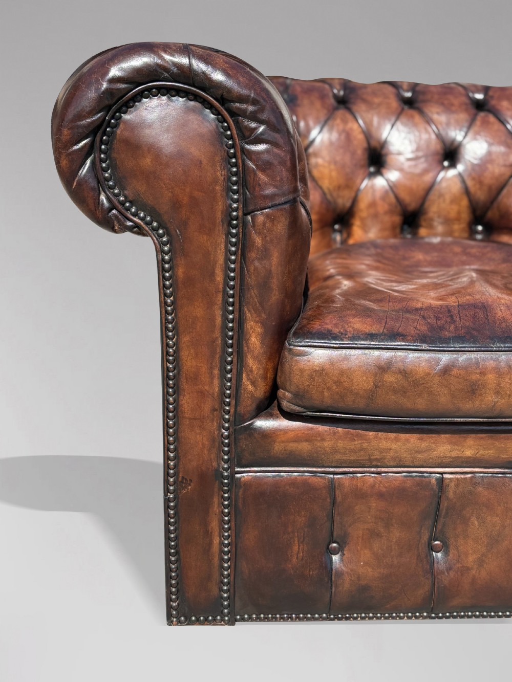An Edwardian brown leather Chesterfield armchair featuring deep button quilting, rolled arms, and stud trim details. View VI