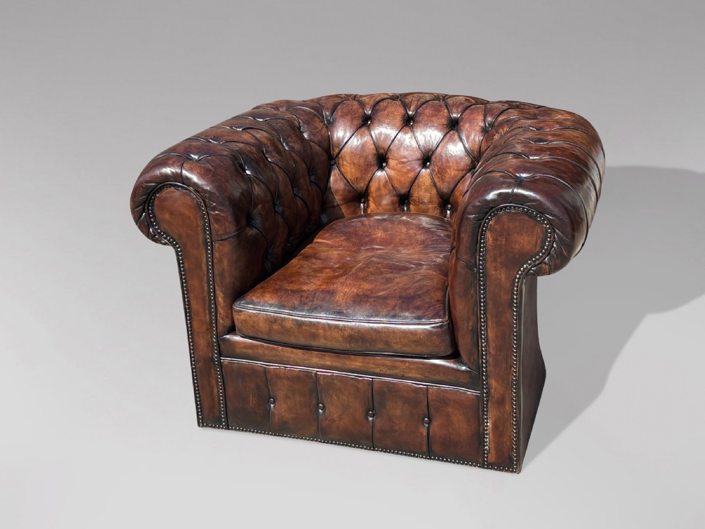 An Edwardian brown leather Chesterfield armchair featuring deep button quilting, rolled arms, and stud trim details. View VIII
