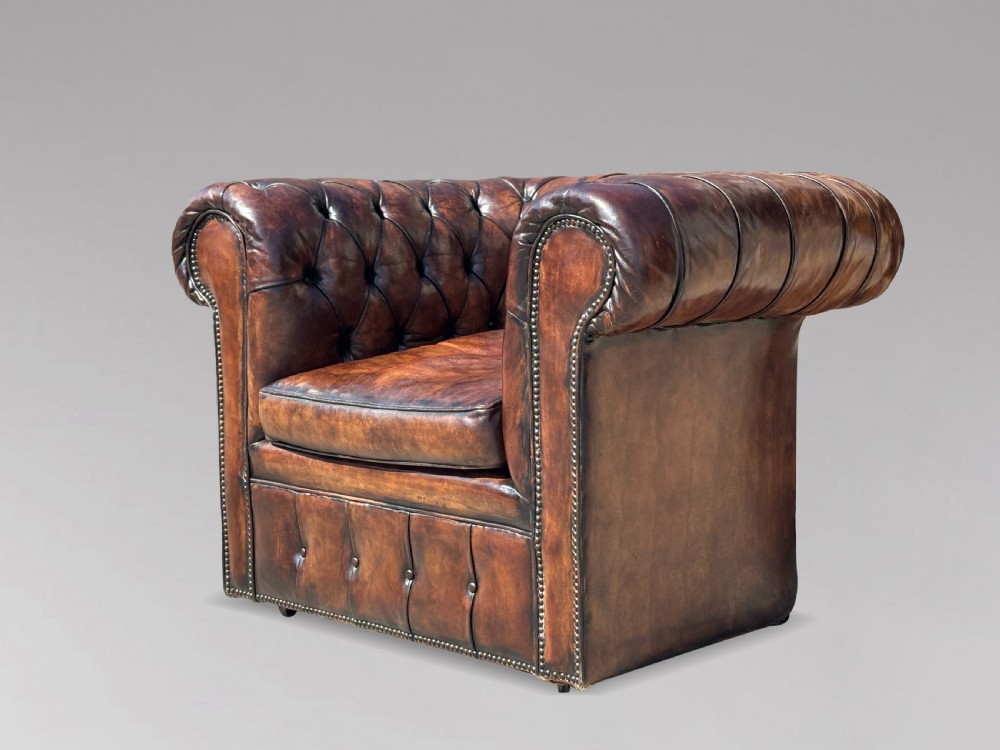 An Edwardian brown leather Chesterfield armchair featuring deep button quilting, rolled arms, and stud trim details. View X