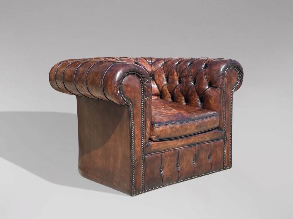 An Edwardian brown leather Chesterfield armchair featuring deep button quilting, rolled arms, and stud trim details. View XII