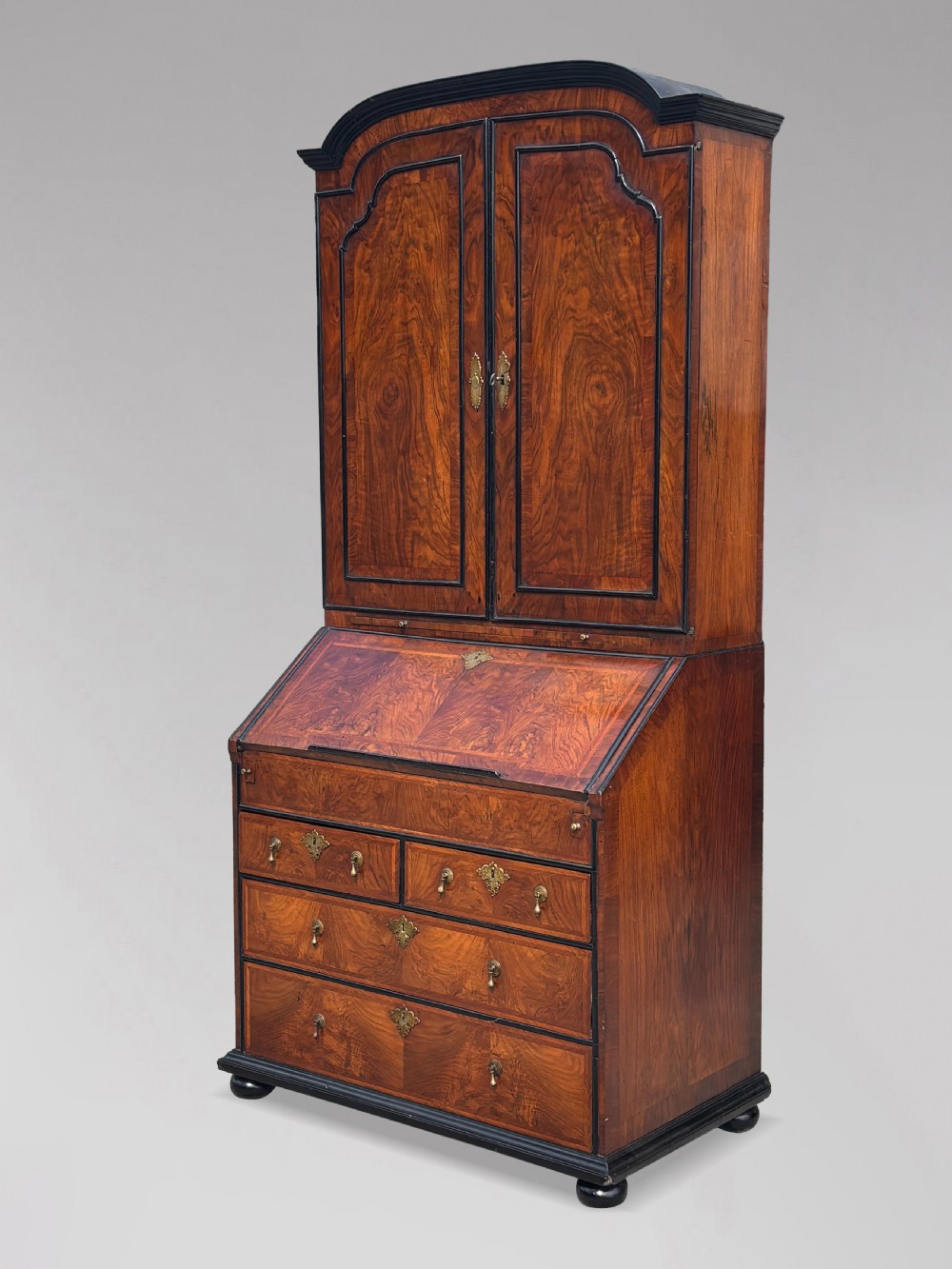 An 18th-century George I walnut bureau bookcase featuring arched panelled upper doors, a slant-front desk, and graduated lower drawers.