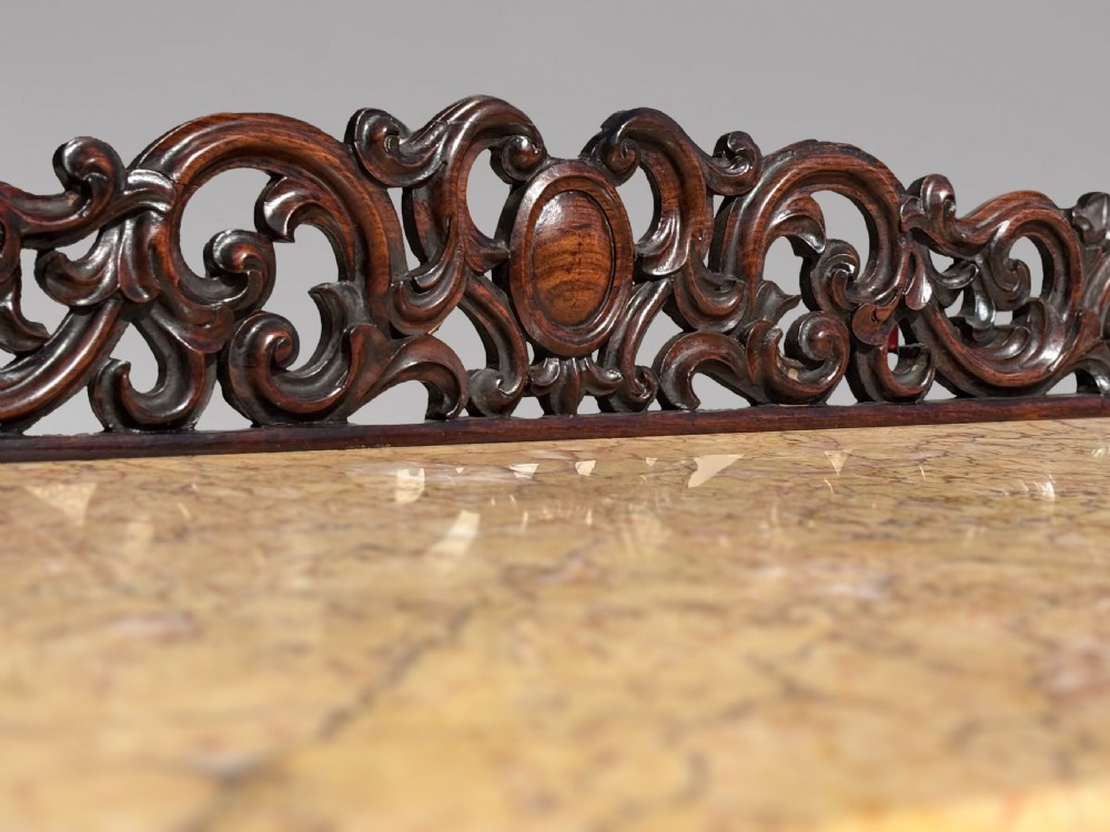 A 19th-century carved rosewood console table featuring a light marble top, elaborate pierced scrollwork frieze, mirrored back panel, and a shaped lower shelf. View V