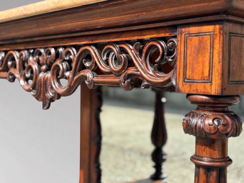 A 19th-century carved rosewood console table featuring a light marble top, elaborate pierced scrollwork frieze, mirrored back panel, and a shaped lower shelf. View XIV