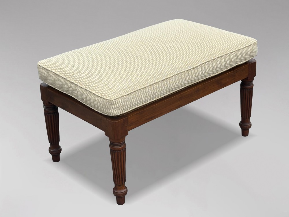 A 19th-century rectangular teak stool with fluted turned legs and a cream textured upholstered cushion top.