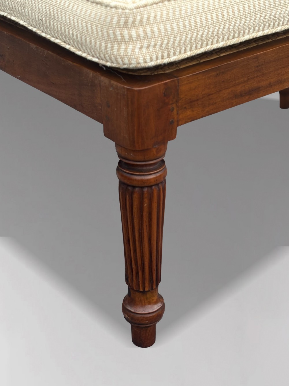 A 19th-century rectangular teak stool with fluted turned legs and a cream textured upholstered cushion top. View VI