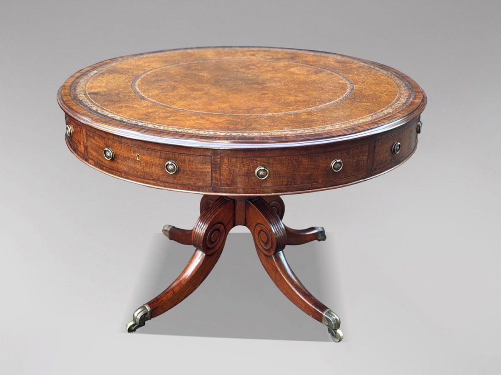 A 19th-century Regency mahogany drum table featuring a circular leather inset top, frieze drawers with brass ring handles, and a carved pedestal with four splayed legs on brass castors.