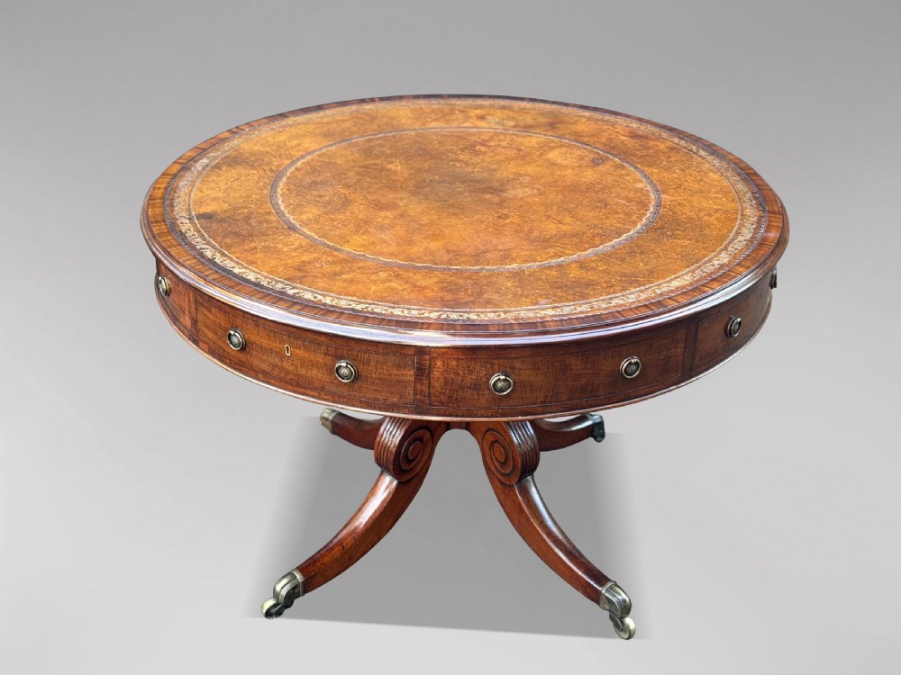 A 19th-century Regency mahogany drum table featuring a circular leather inset top, frieze drawers with brass ring handles, and a carved pedestal with four splayed legs on brass castors. View II