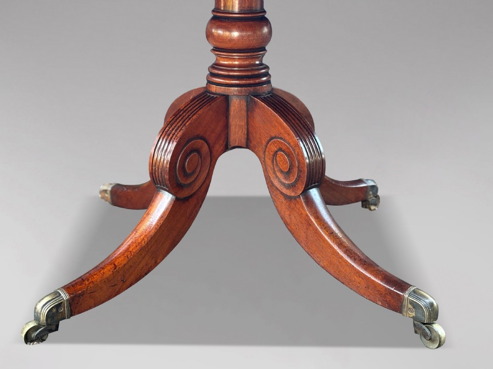 A 19th-century Regency mahogany drum table featuring a circular leather inset top, frieze drawers with brass ring handles, and a carved pedestal with four splayed legs on brass castors. View III