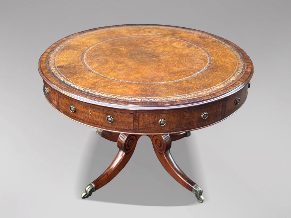 A 19th-century Regency mahogany drum table featuring a circular leather inset top, frieze drawers with brass ring handles, and a carved pedestal with four splayed legs on brass castors. View IV