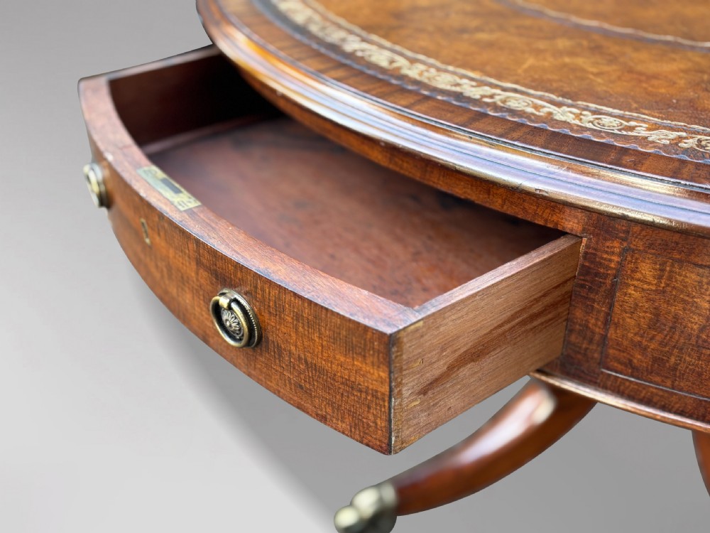 A 19th-century Regency mahogany drum table featuring a circular leather inset top, frieze drawers with brass ring handles, and a carved pedestal with four splayed legs on brass castors. View VI