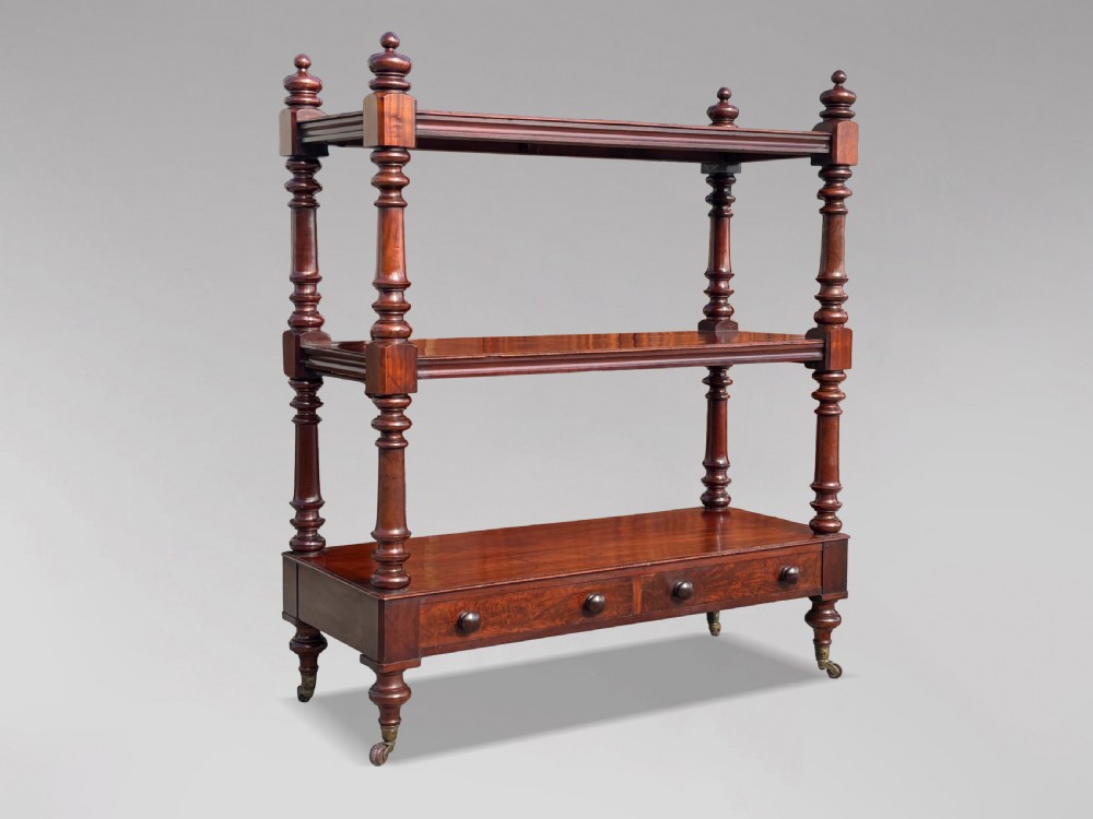 A nineteenth-century three-tiered mahogany dumb waiter with turned support columns, two drawers at the base, and brass castors. View II