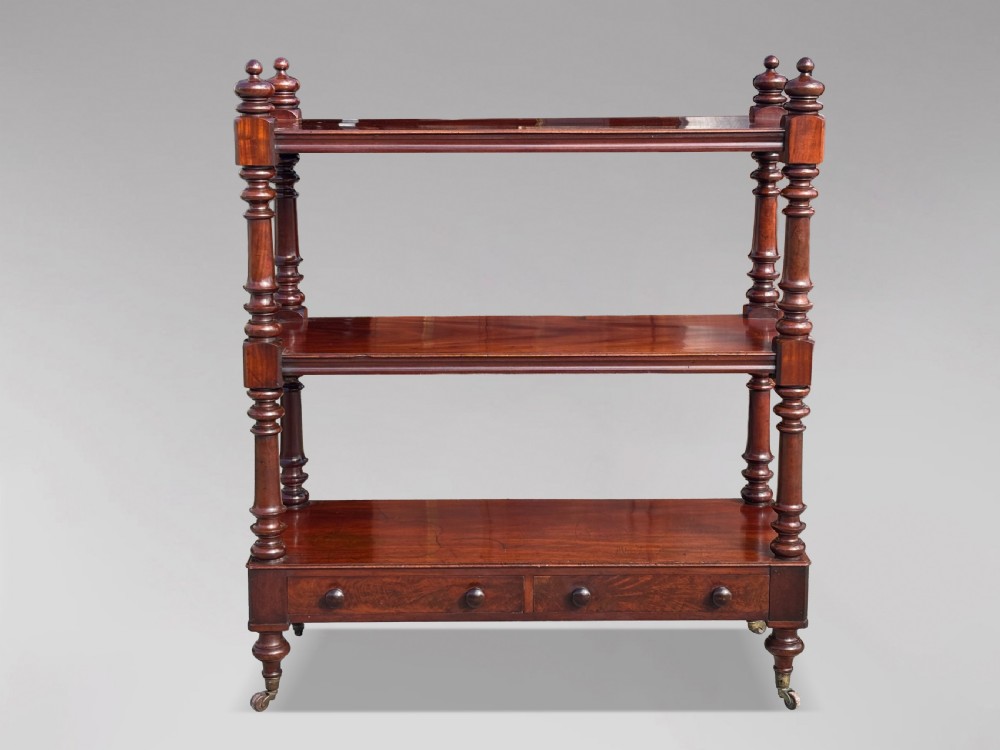 A nineteenth-century three-tiered mahogany dumb waiter with turned support columns, two drawers at the base, and brass castors. View III