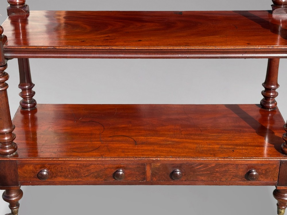 A nineteenth-century three-tiered mahogany dumb waiter with turned support columns, two drawers at the base, and brass castors. View V