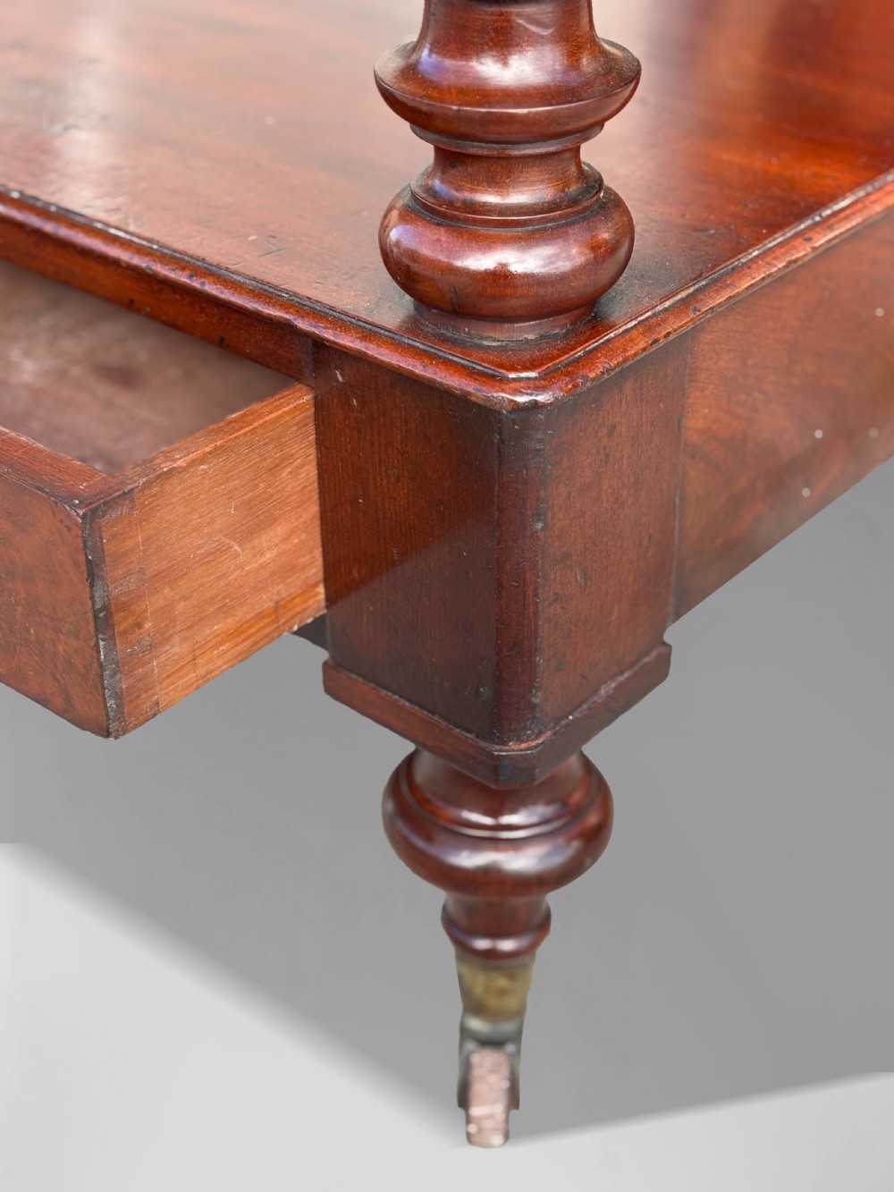 A nineteenth-century three-tiered mahogany dumb waiter with turned support columns, two drawers at the base, and brass castors. View VI