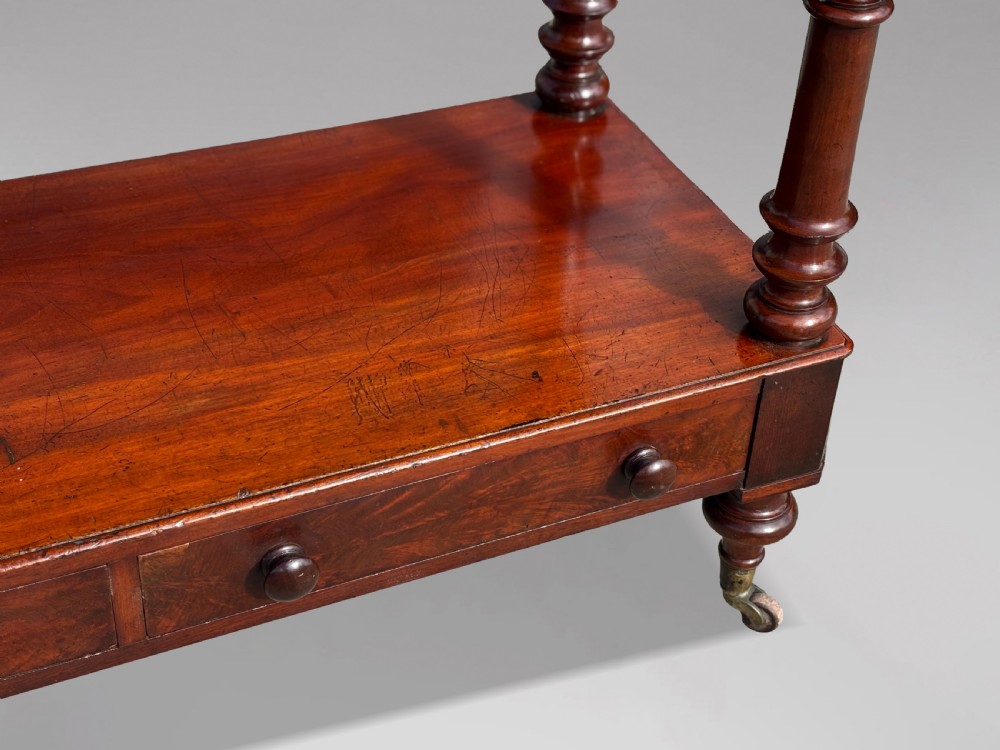 A nineteenth-century three-tiered mahogany dumb waiter with turned support columns, two drawers at the base, and brass castors. View VIII