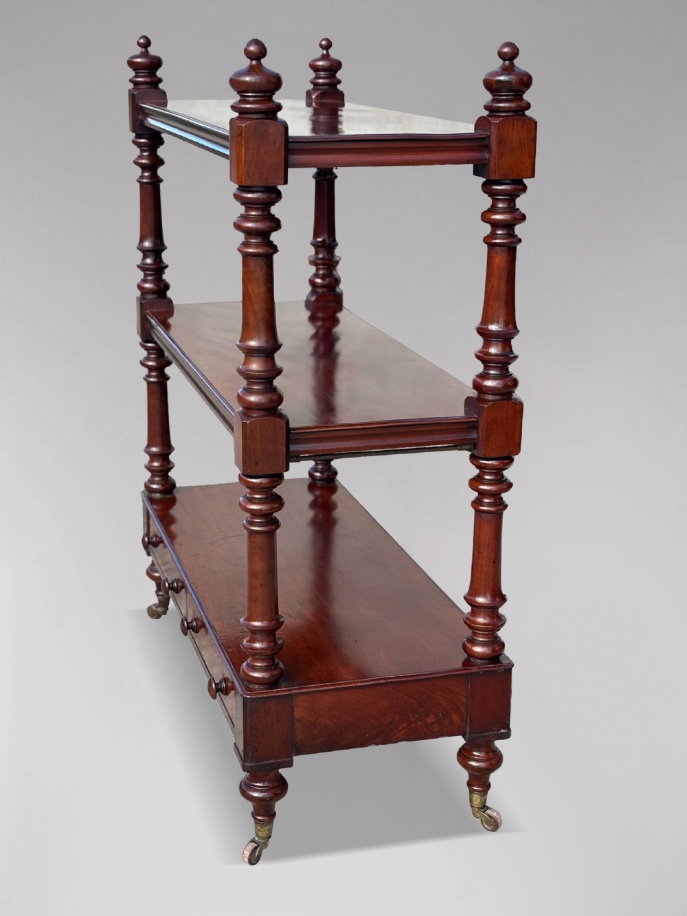 A nineteenth-century three-tiered mahogany dumb waiter with turned support columns, two drawers at the base, and brass castors. View X