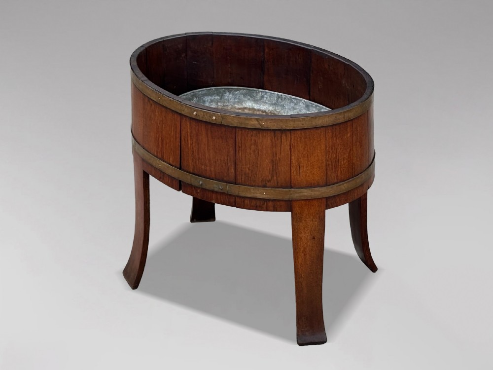 An 18th-century George III oval staved walnut wine cooler featuring twin brass binding bands, splayed legs, and an internal metal liner.