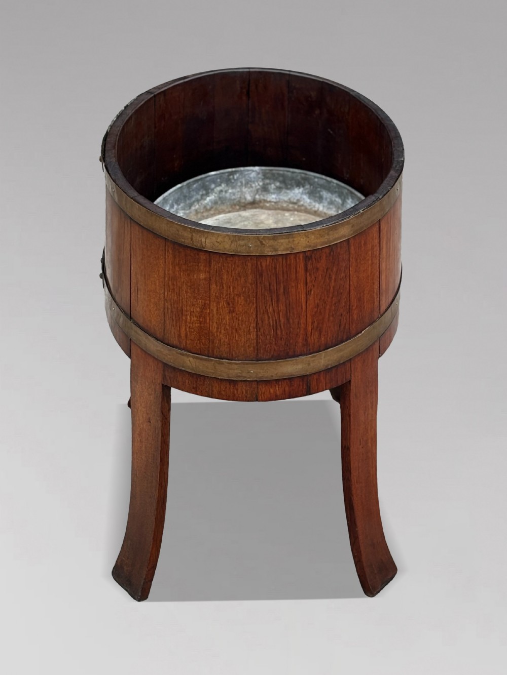 An 18th-century George III oval staved walnut wine cooler featuring twin brass binding bands, splayed legs, and an internal metal liner. View IV