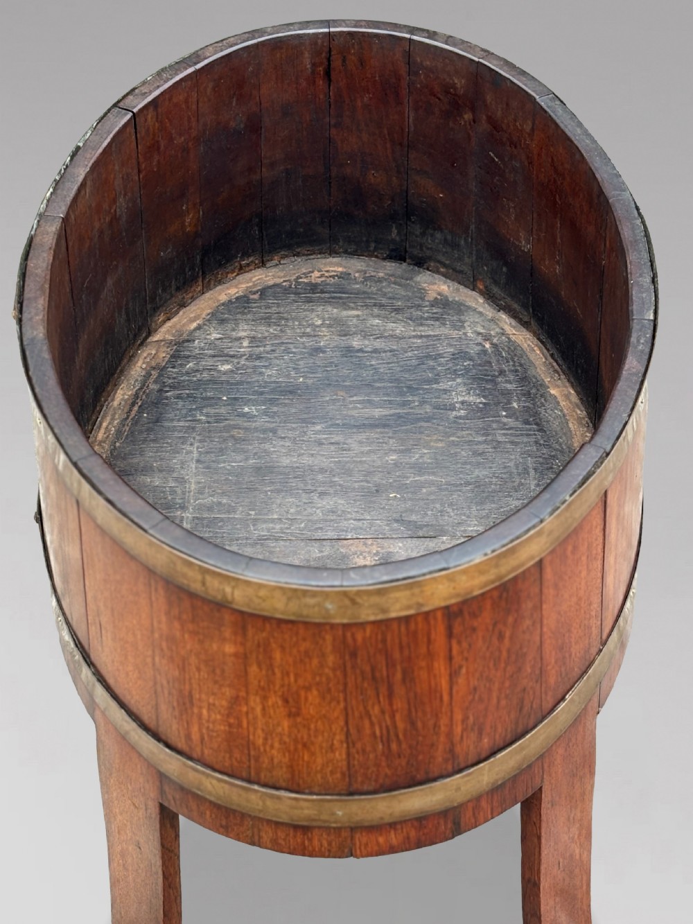 An 18th-century George III oval staved walnut wine cooler featuring twin brass binding bands, splayed legs, and an internal metal liner. View V