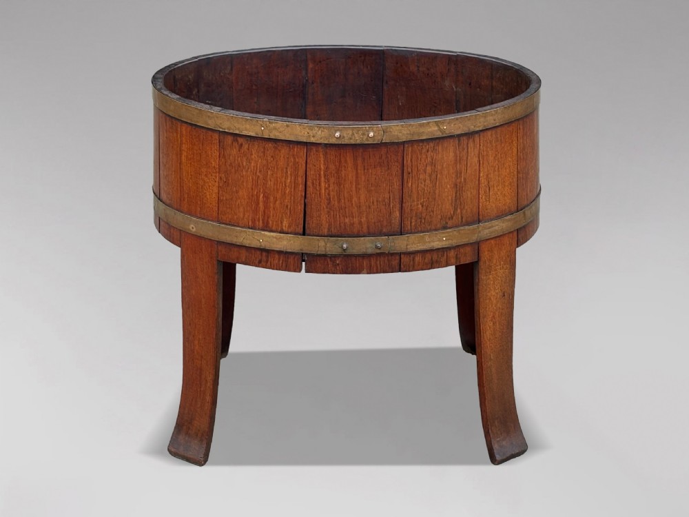 An 18th-century George III oval staved walnut wine cooler featuring twin brass binding bands, splayed legs, and an internal metal liner. View IX