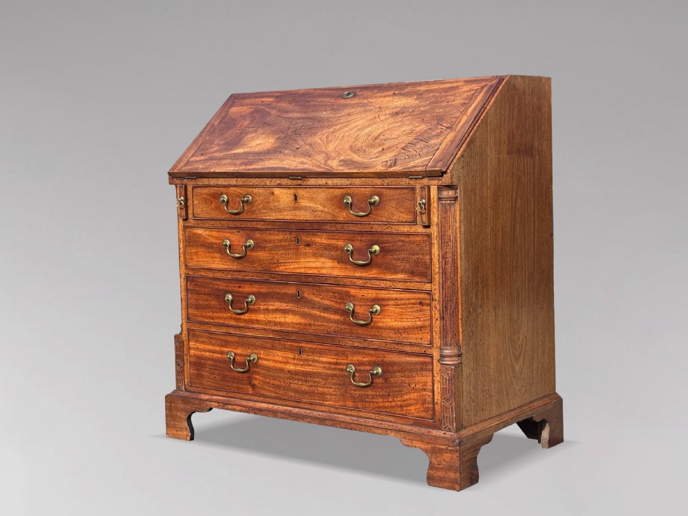 An 18th-century George III mahogany bureau featuring a sloping fall-front writing flap above four graduated drawers with brass handles and bracket feet.