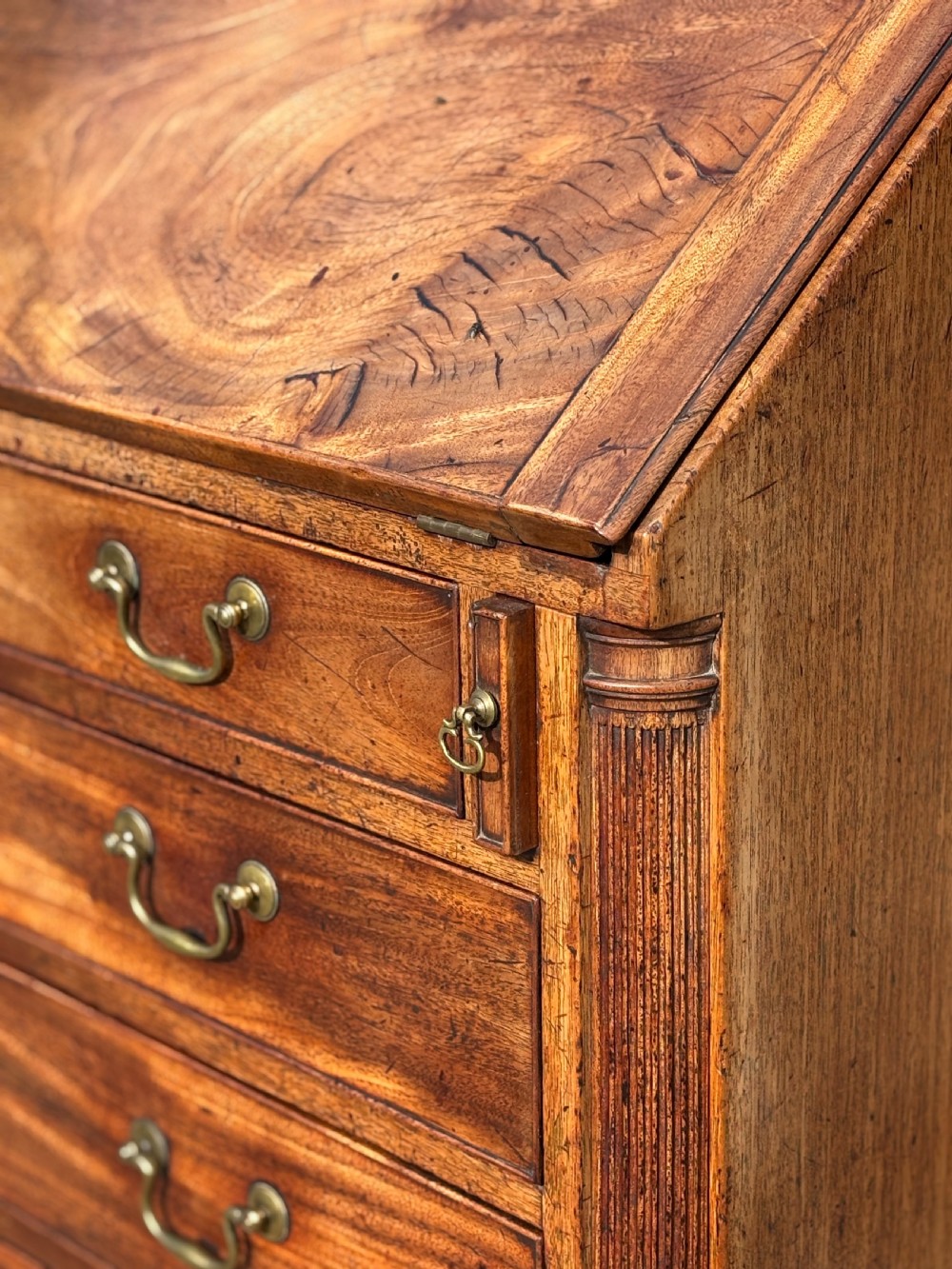 An 18th-century George III mahogany bureau featuring a sloping fall-front writing flap above four graduated drawers with brass handles and bracket feet. View V