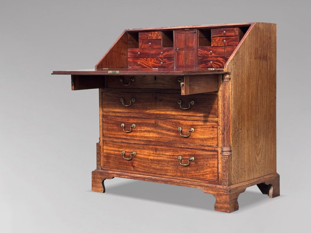 An 18th-century George III mahogany bureau featuring a sloping fall-front writing flap above four graduated drawers with brass handles and bracket feet. View X