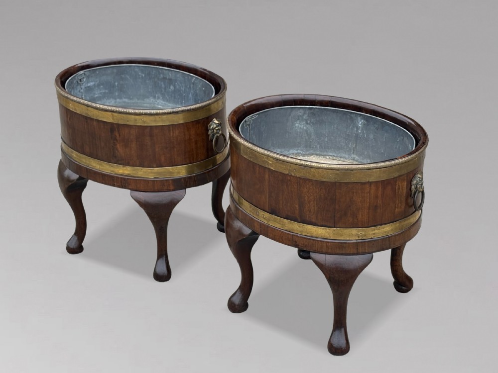 A pair of oval eighteenth-century Georgian mahogany wine coolers featuring brass banding, lion mask drop handles, metal liners, and cabriole legs.