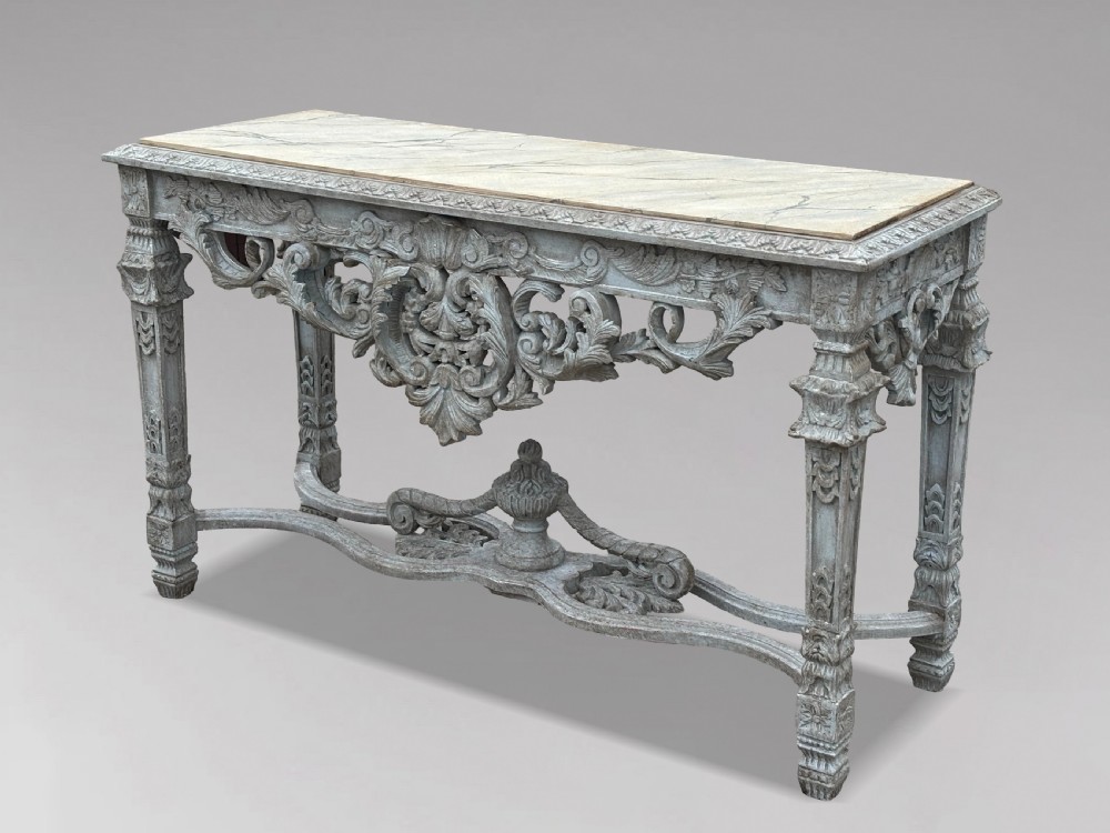 A carved Louis XIV style grey painted console table with an intricate aproned skirt, stretcher base, and faux marble top.