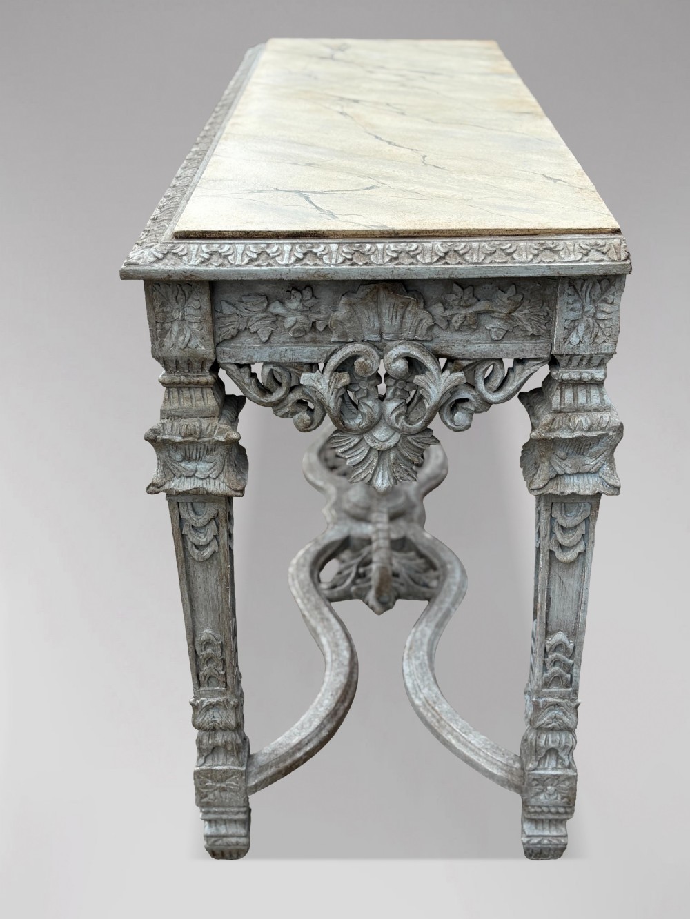 A carved Louis XIV style grey painted console table with an intricate aproned skirt, stretcher base, and faux marble top. View IX