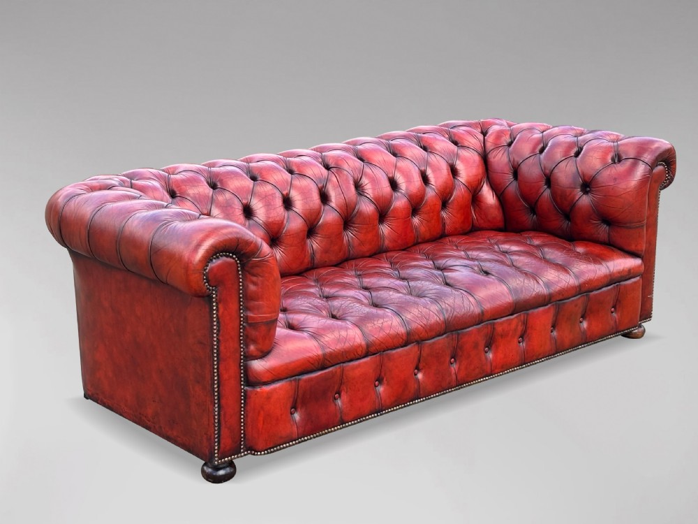 An antique three-seater Chesterfield sofa upholstered in deep red buttoned leather with rolled arms and brass studding.