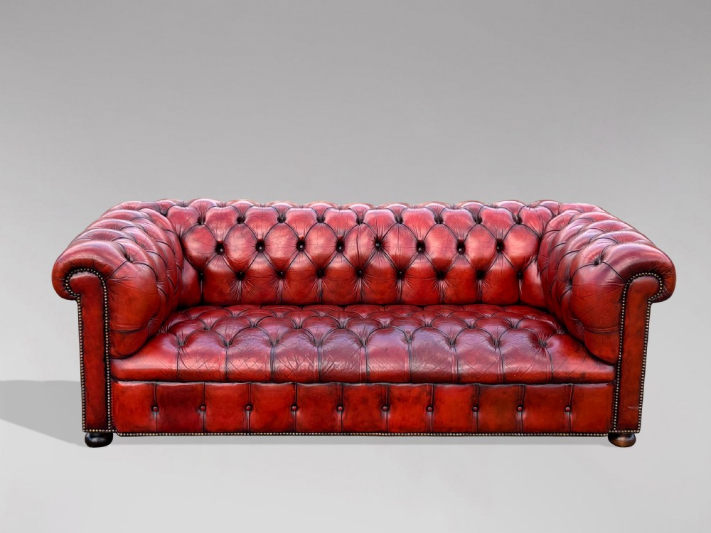 An antique three-seater Chesterfield sofa upholstered in deep red buttoned leather with rolled arms and brass studding. View II