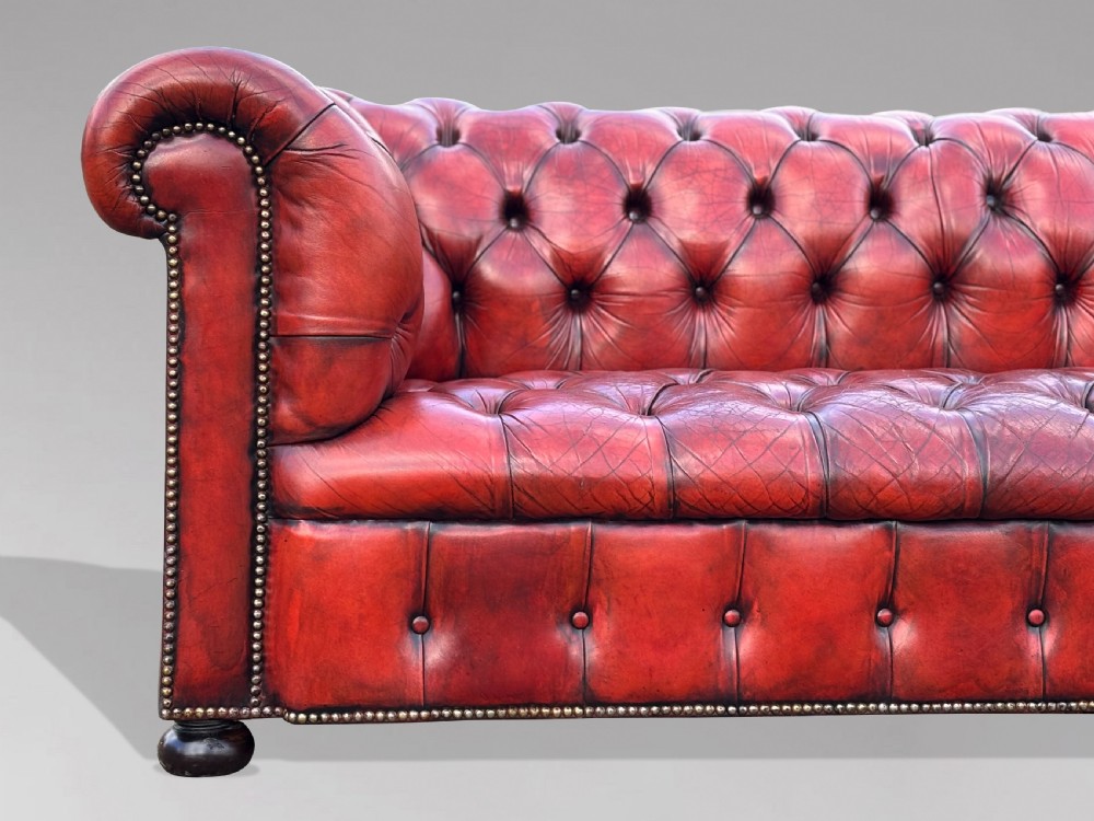 An antique three-seater Chesterfield sofa upholstered in deep red buttoned leather with rolled arms and brass studding. View III
