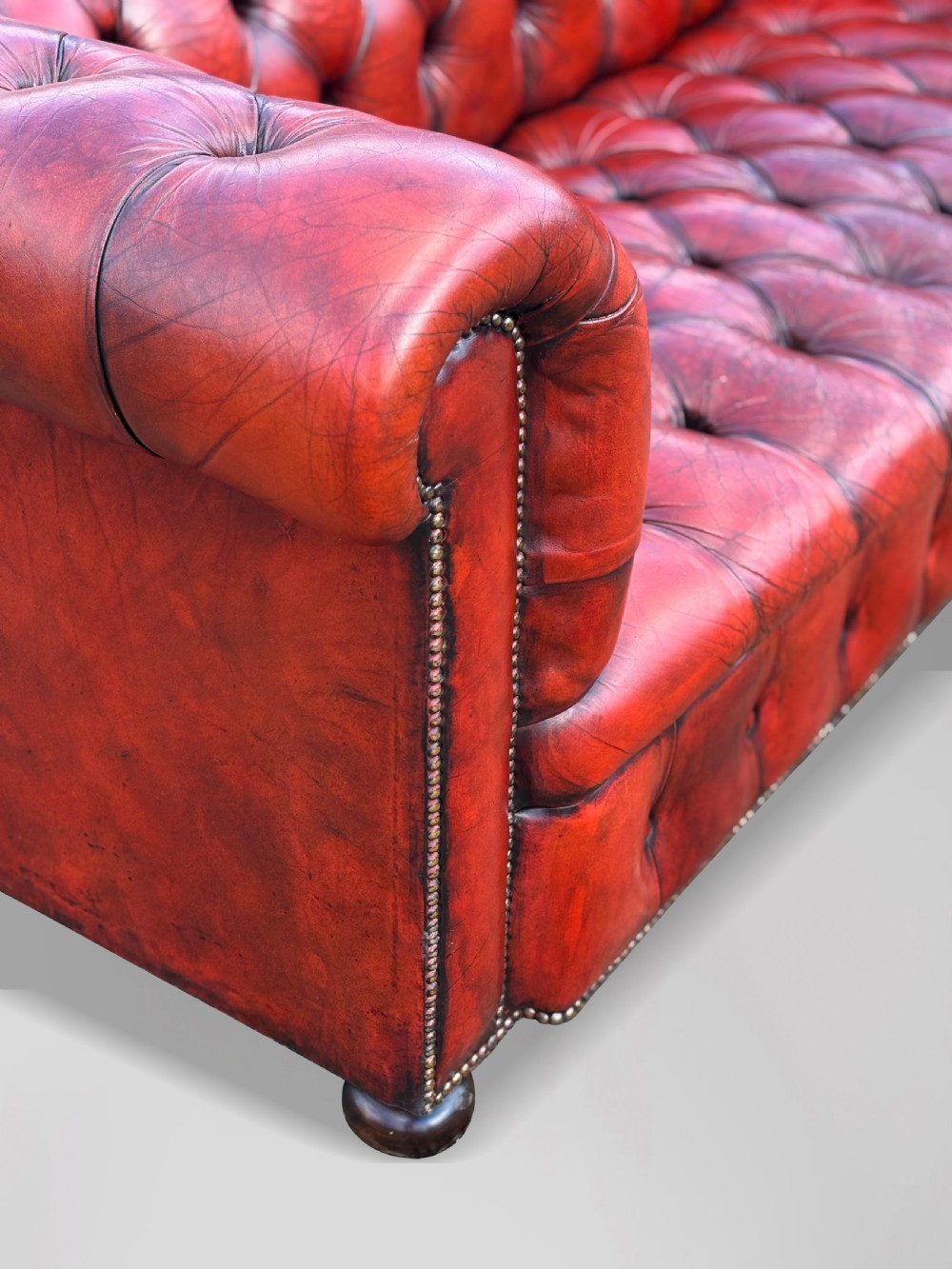 An antique three-seater Chesterfield sofa upholstered in deep red buttoned leather with rolled arms and brass studding. View IV