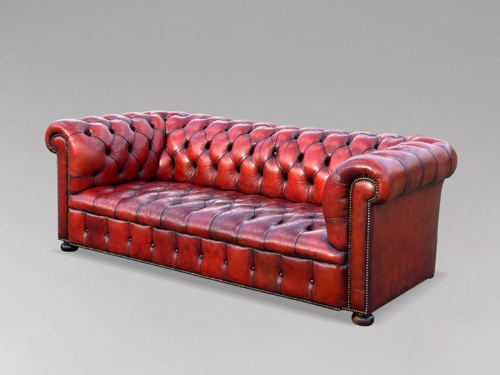 An antique three-seater Chesterfield sofa upholstered in deep red buttoned leather with rolled arms and brass studding. View VI