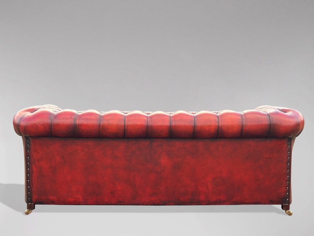 An antique three-seater Chesterfield sofa upholstered in deep red buttoned leather with rolled arms and brass studding. View VII