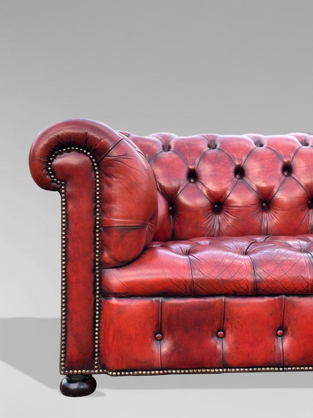 An antique three-seater Chesterfield sofa upholstered in deep red buttoned leather with rolled arms and brass studding. View VIII